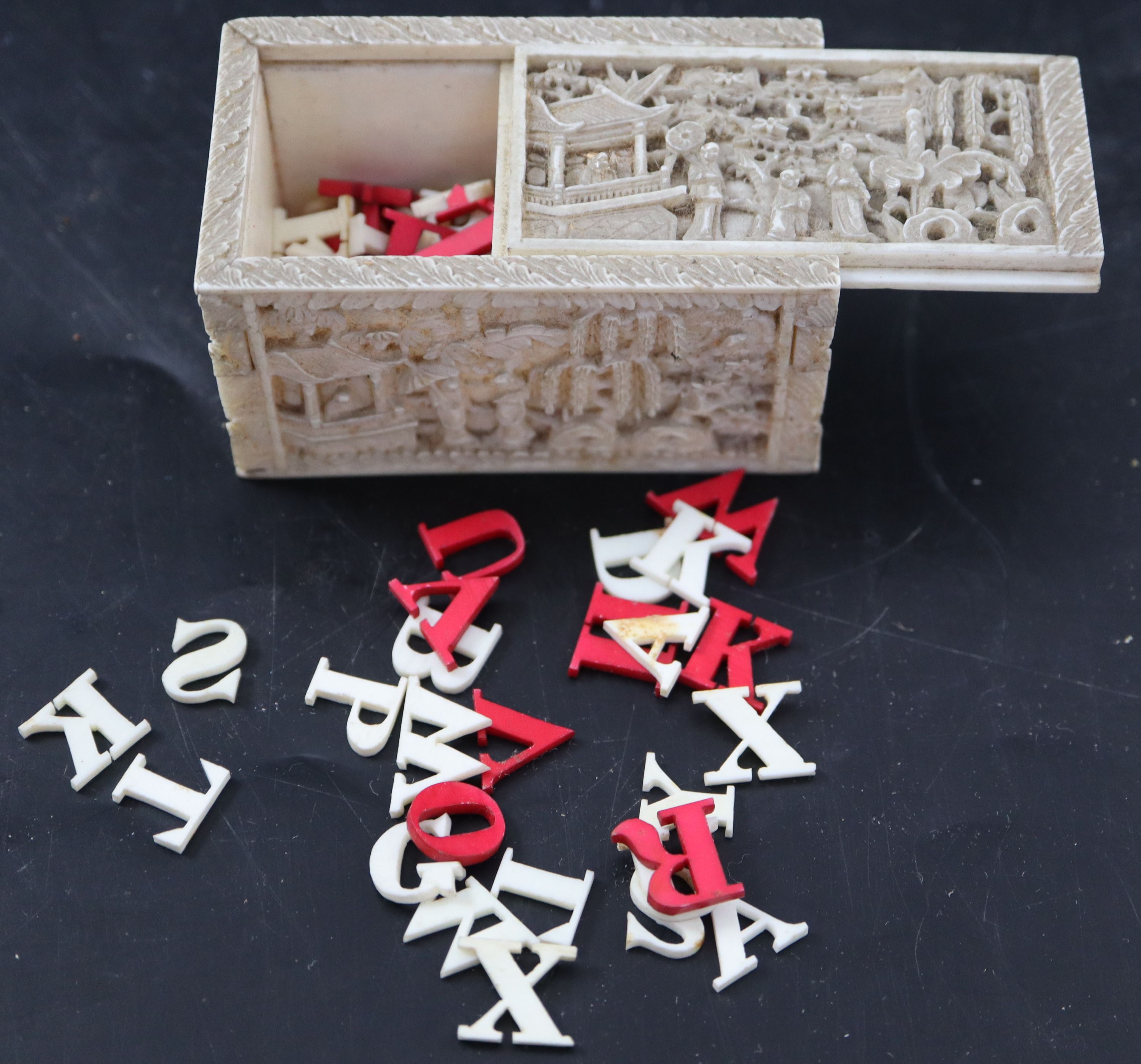 A 19th century Chinese relief carved ivory box housing plain and red stained ivory alphabet letters, 6.75cm